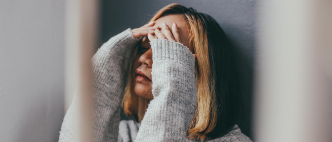 Mujer joven apoyada en la pared manos en la cabeza triste y pensativa