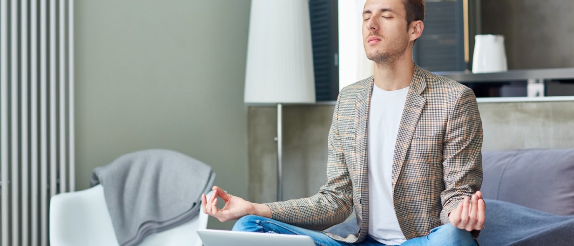 Hombre joven con chaqueta a cuadros meditando delante de su portátil en el sofá