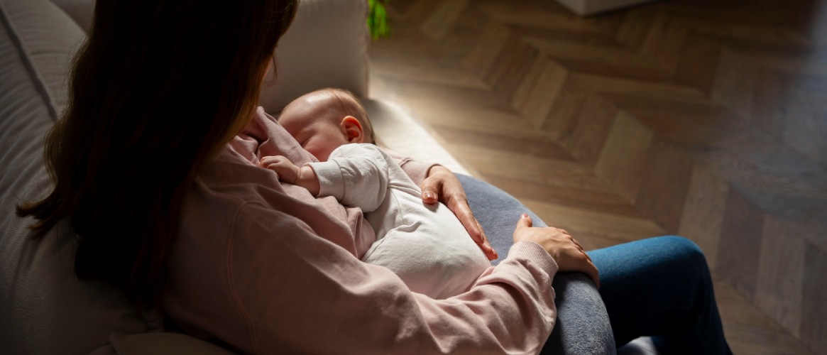 Mujer dando de mamar a su bebé sentada en el sofá