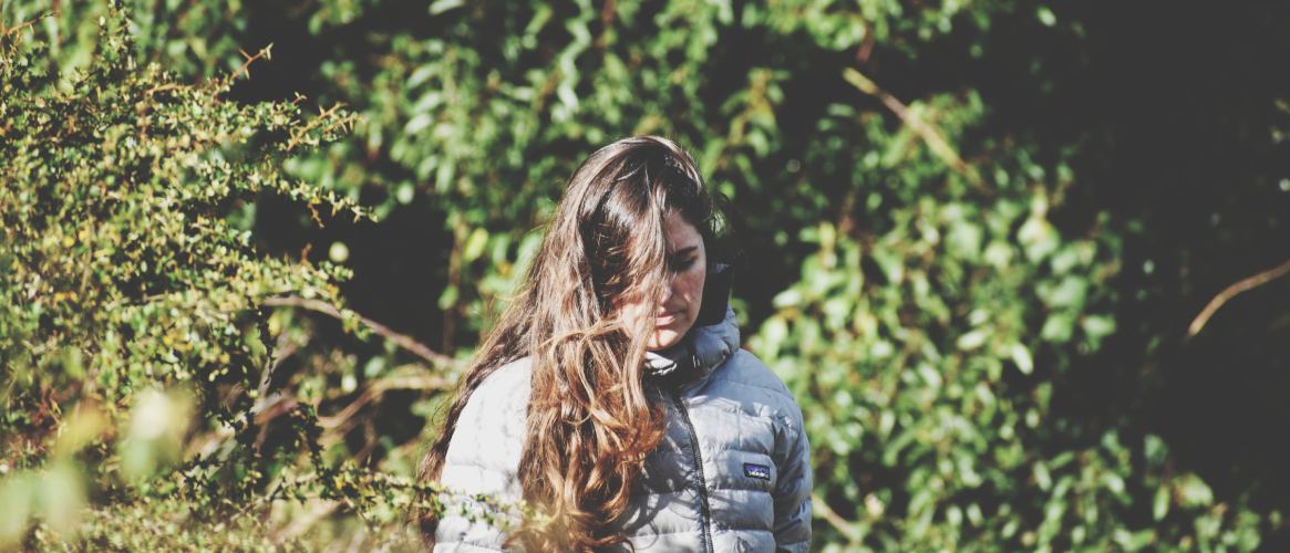 Mujer pelo castaño mirando al suelo en plena naturaleza