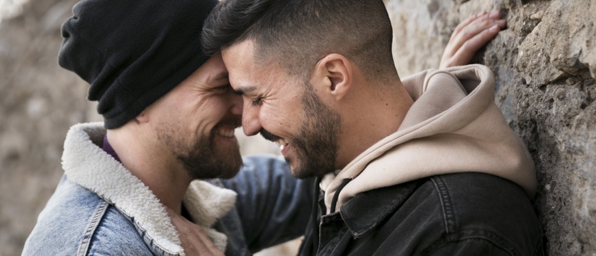 Pareja de dos chicos enamorados sonriendo apoyados en una pared de rocas