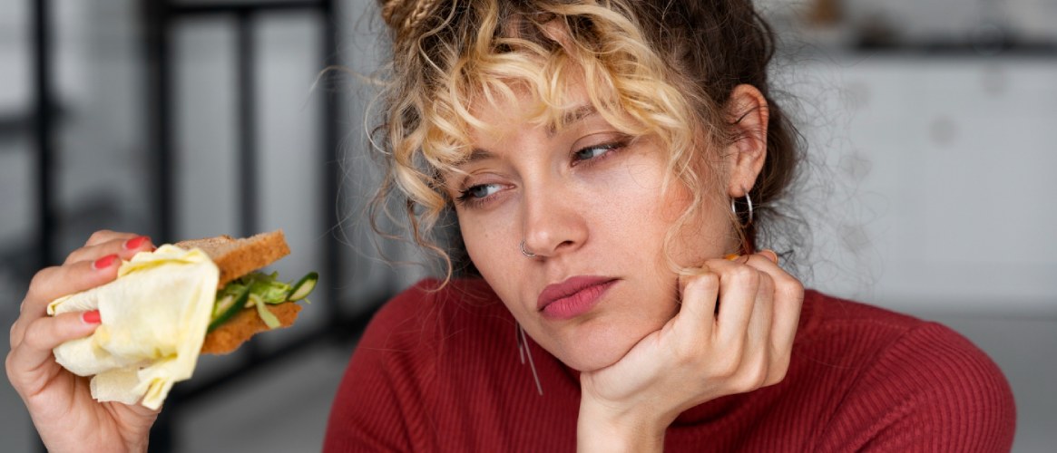 Chica joven mirando un sándwich que tiene en mano