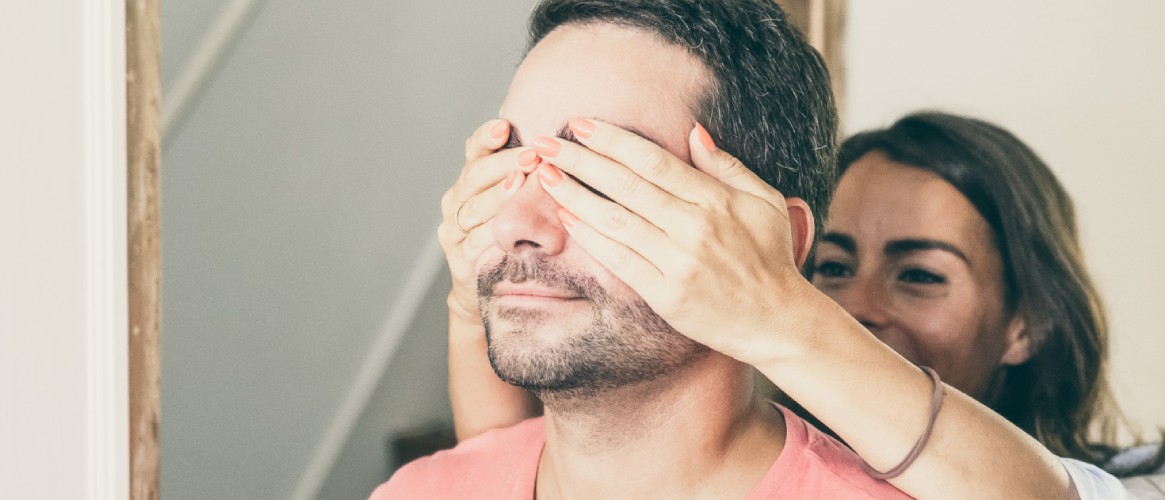 chica joven tapándole los ojos a su novio ella sonríe chico serio