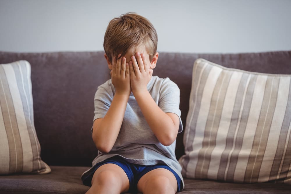 Niño molesto sentado en un sofá gris con las manos en la cara