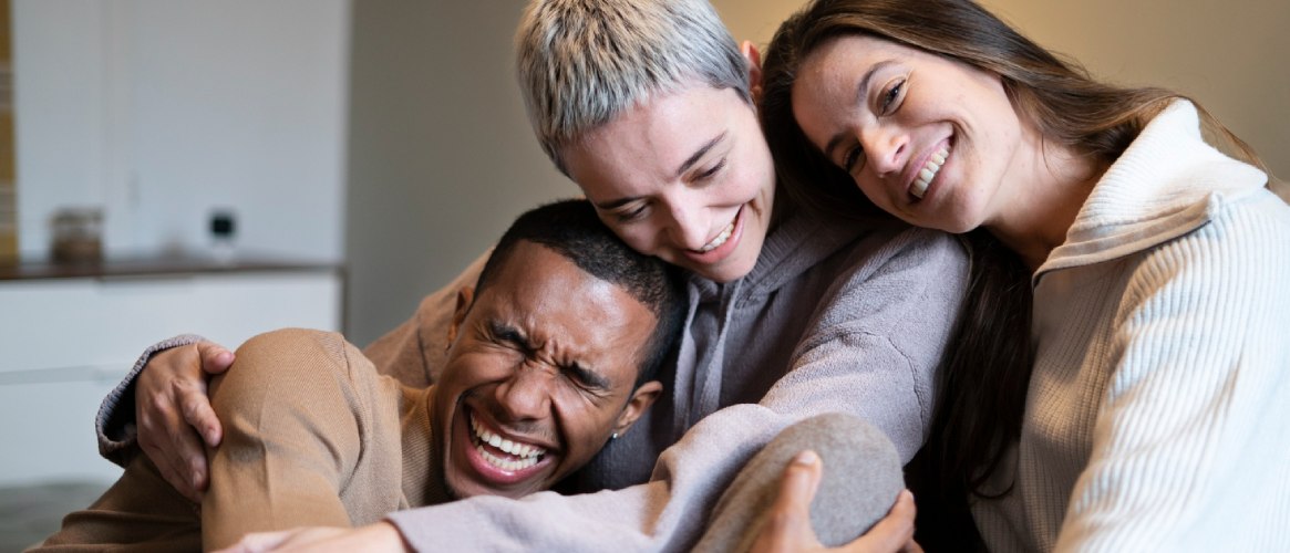Un chico y dos chicas jóvenes abrazados sonriendo