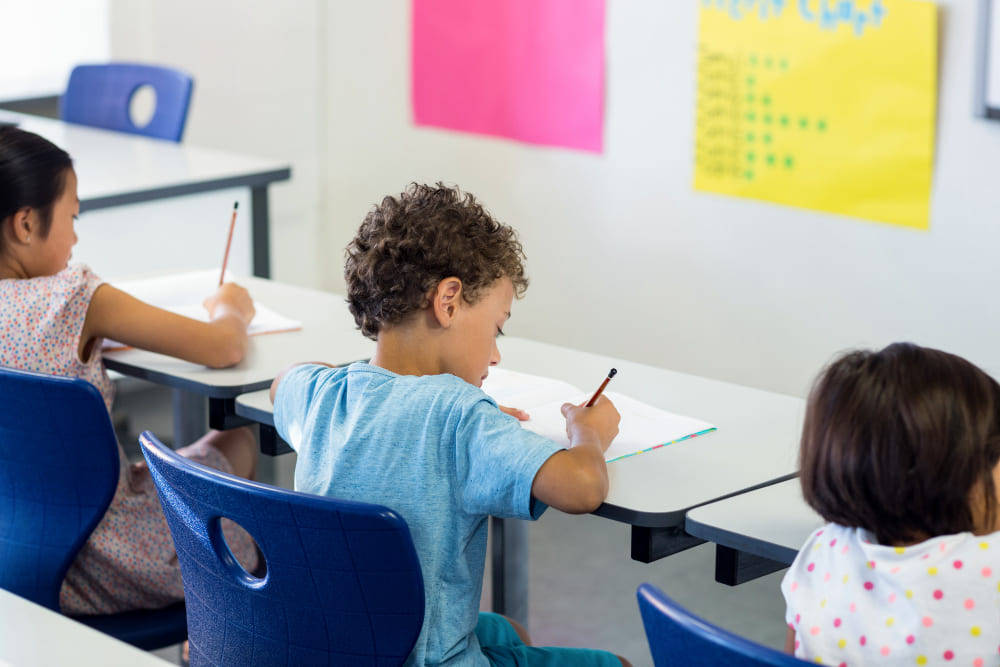 Tres niños pequeños escribiendo en el pupitre de clase.